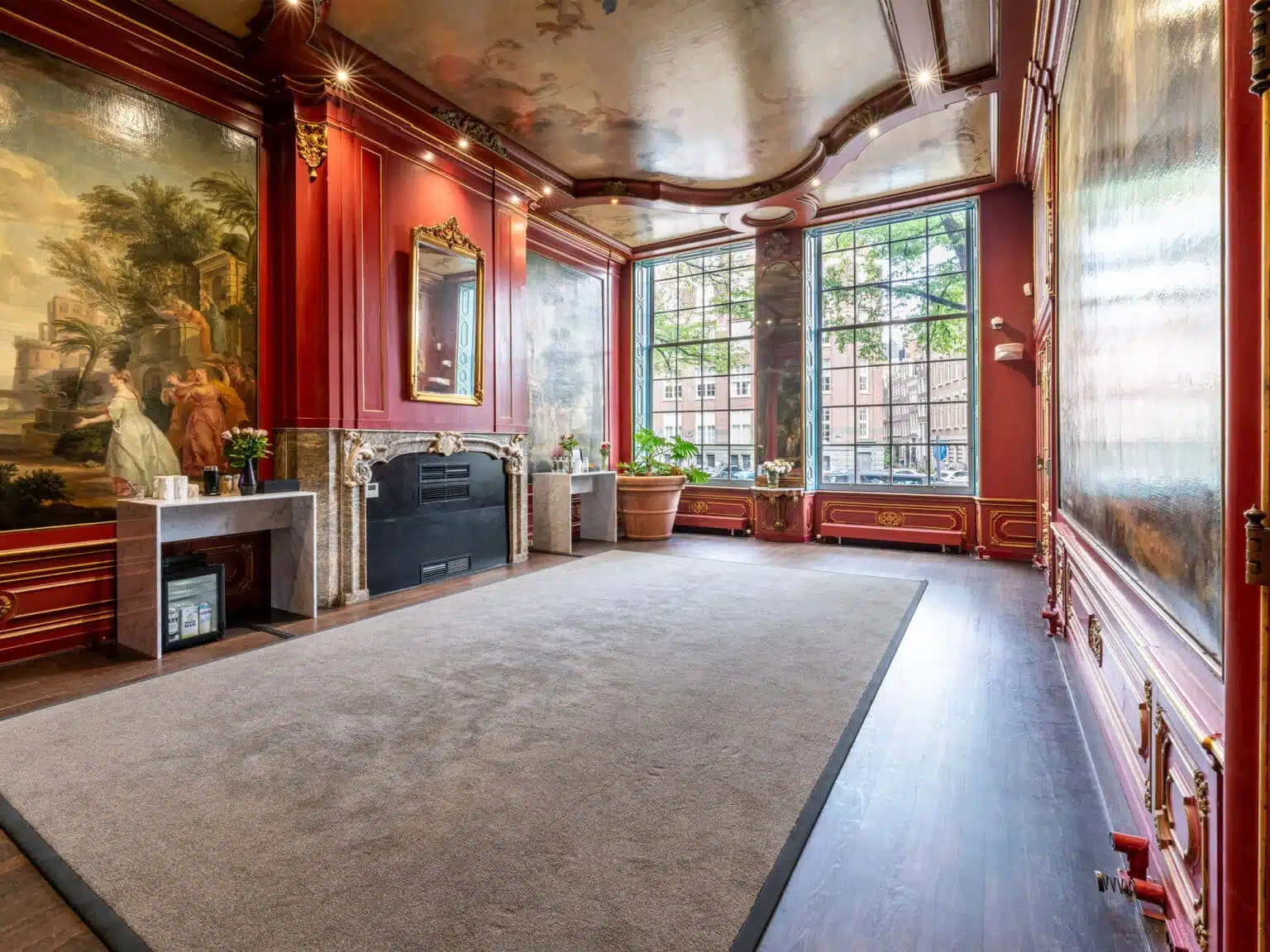 Mindspace Herengracht Amsterdam salon with burgundy walls, gold trim, classical murals, marble fireplace, and tall windows onto the street